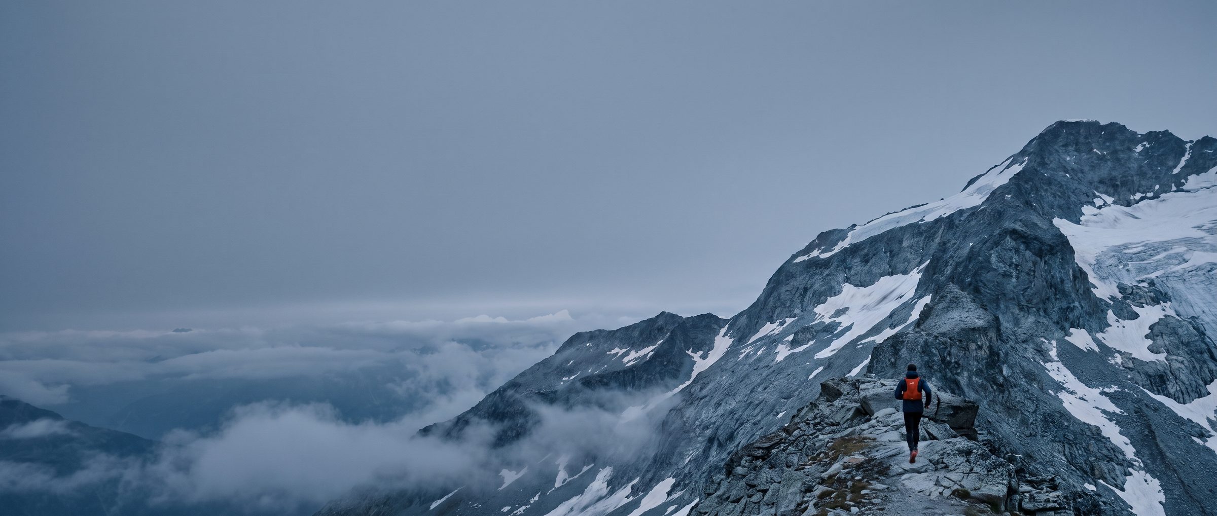 Lone trail runner on a Swiss alpine ridge at daybreak, clouds below the crest